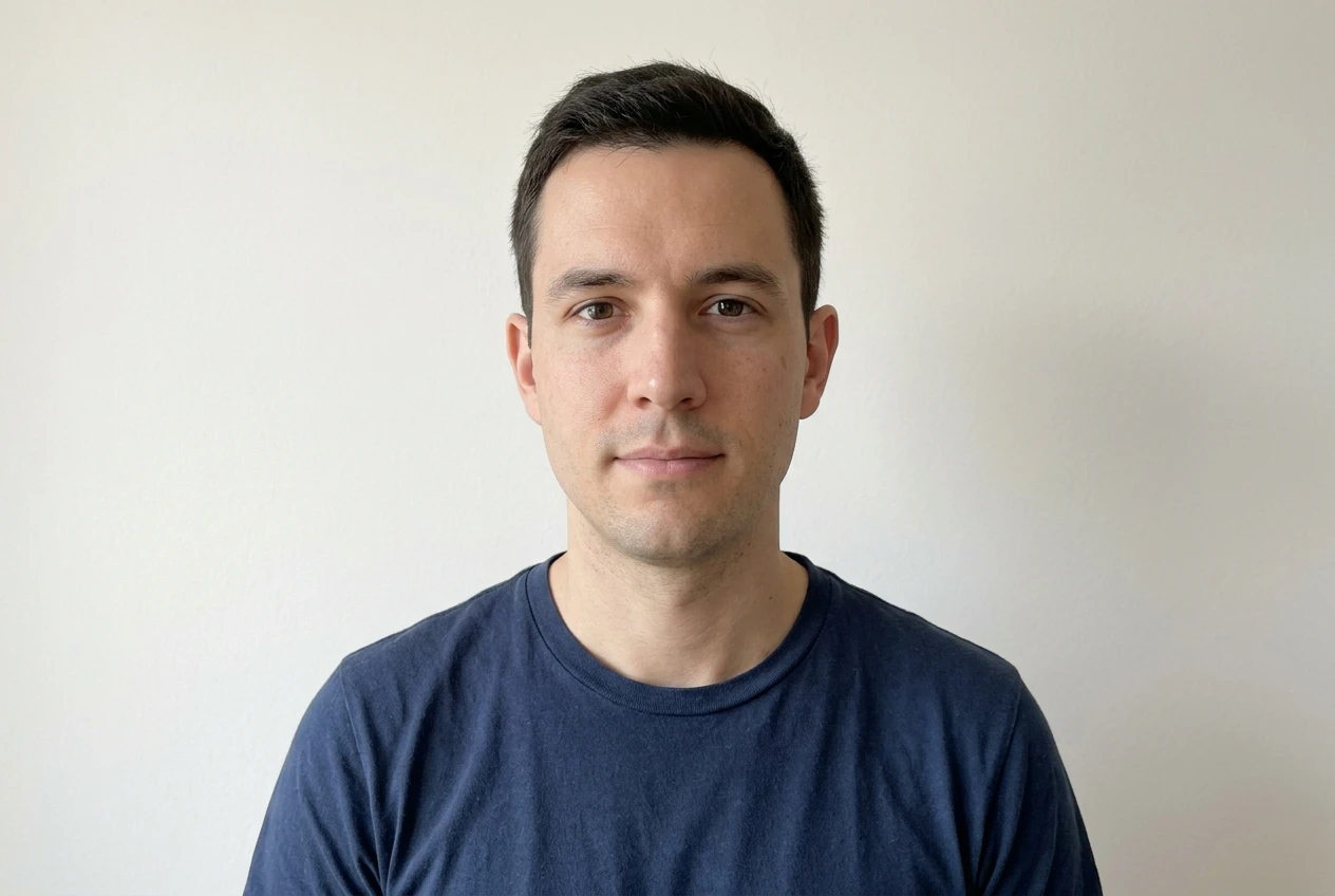 A simple phone-camera headshot example: even daylight on the face, a near-level angle, a plain wall background, and a calm neutral expression, shown as the kind of source photo that transforms cleanly.
